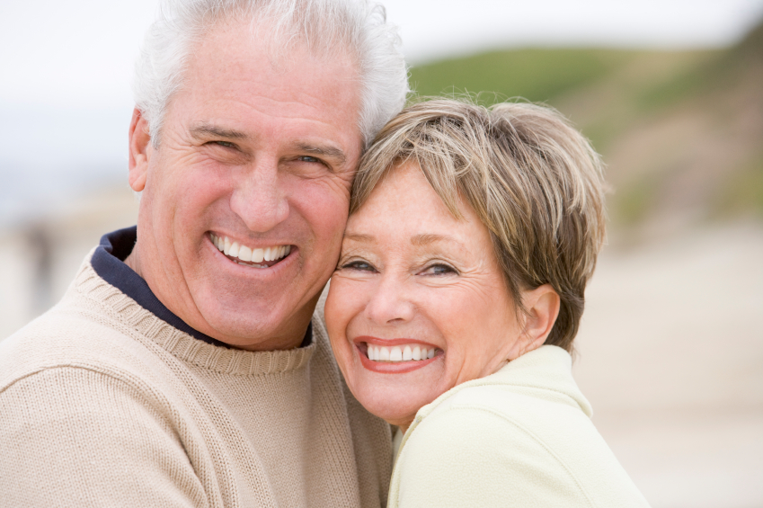 A mature couple smiling together on the beach thanks to restorative dentistry in Alexandria.