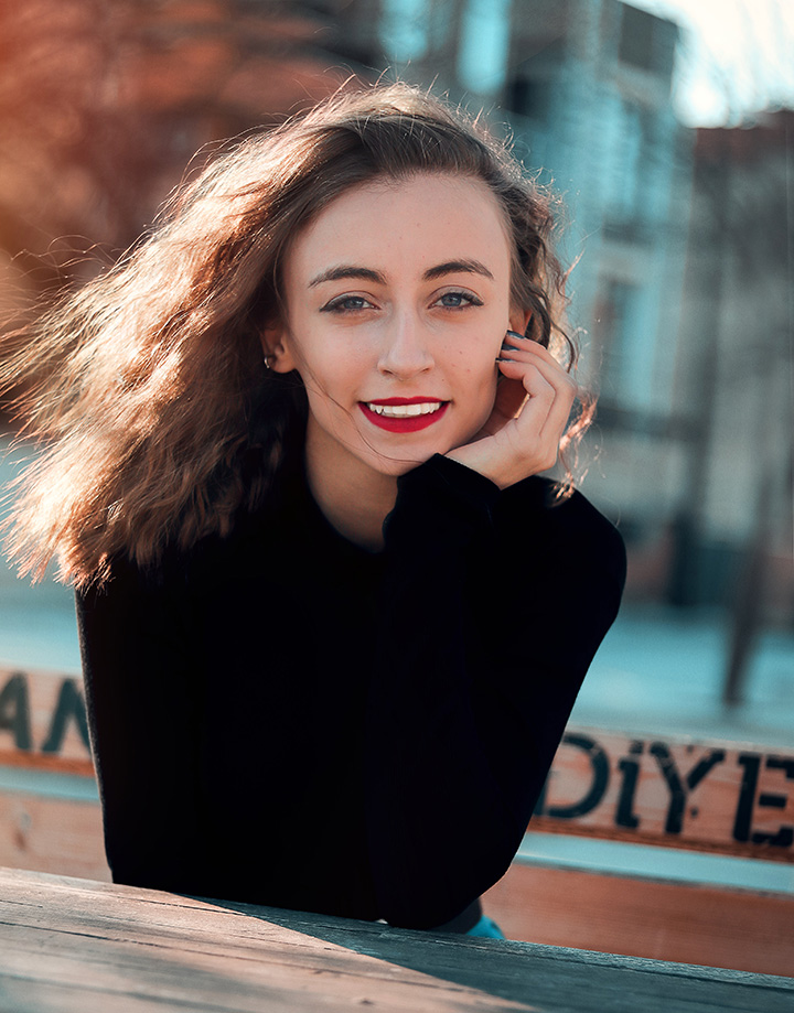 A young woman in a black sweater, smiling confidently after Invisalign treatment.