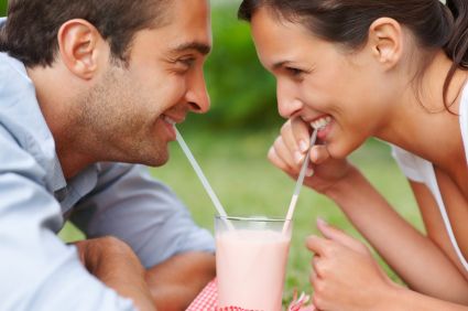 A young couple smiling at each other over a milkshake after teeth whitening treatments in Alexandria.