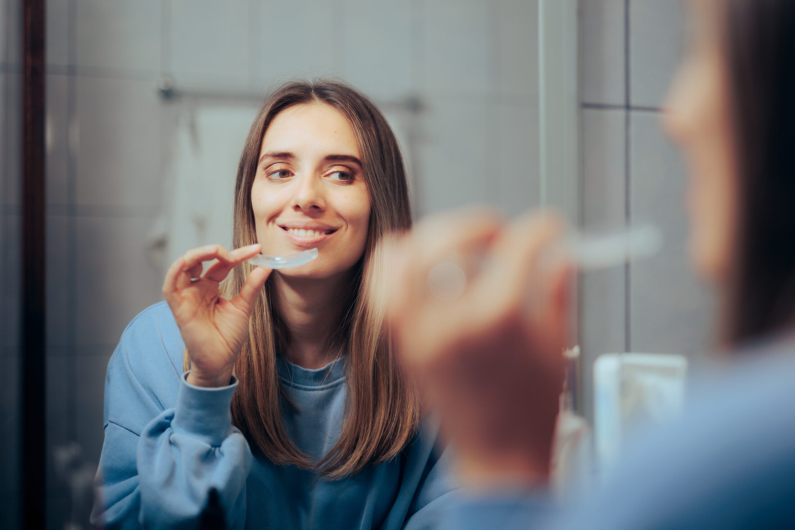 young woman looking in the mirror, clear aligners in hand
