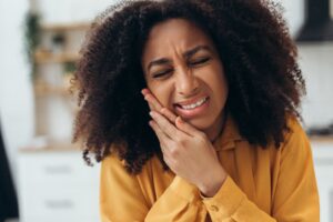 young woman in yellow shirt holding jaw, serious tooth pain